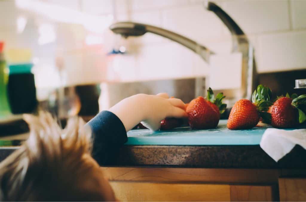 Child reaching for strawberries on kitchen counter
