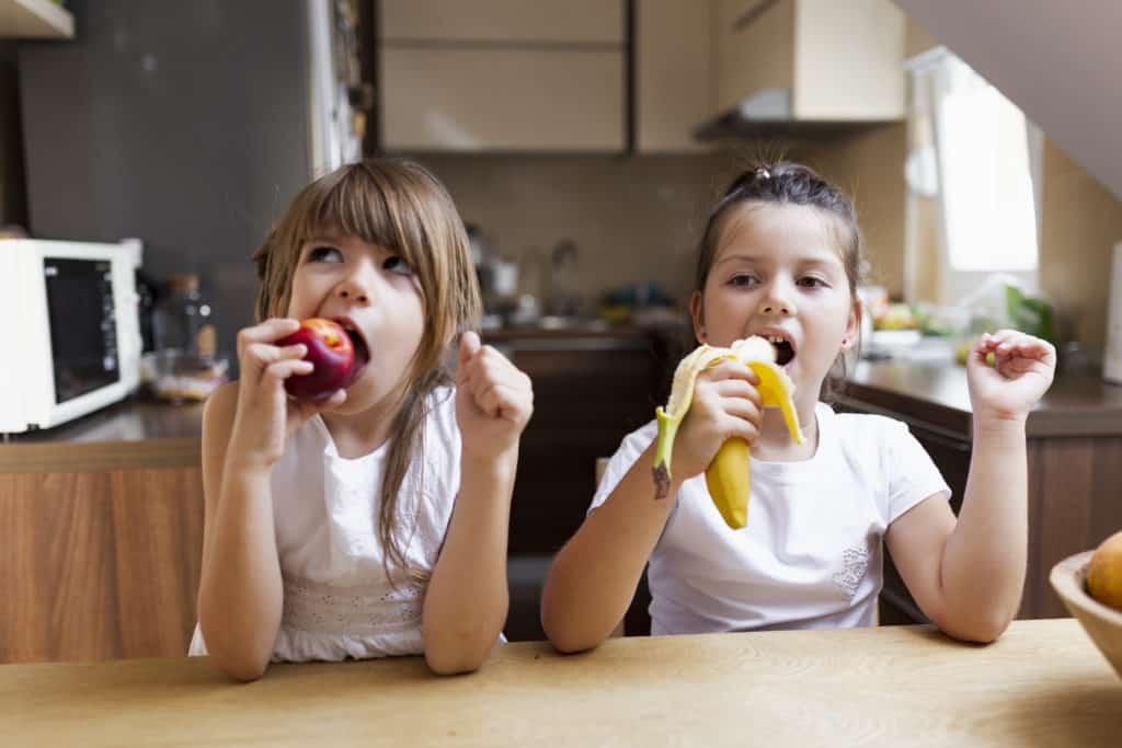 Two kids snacking on fruit