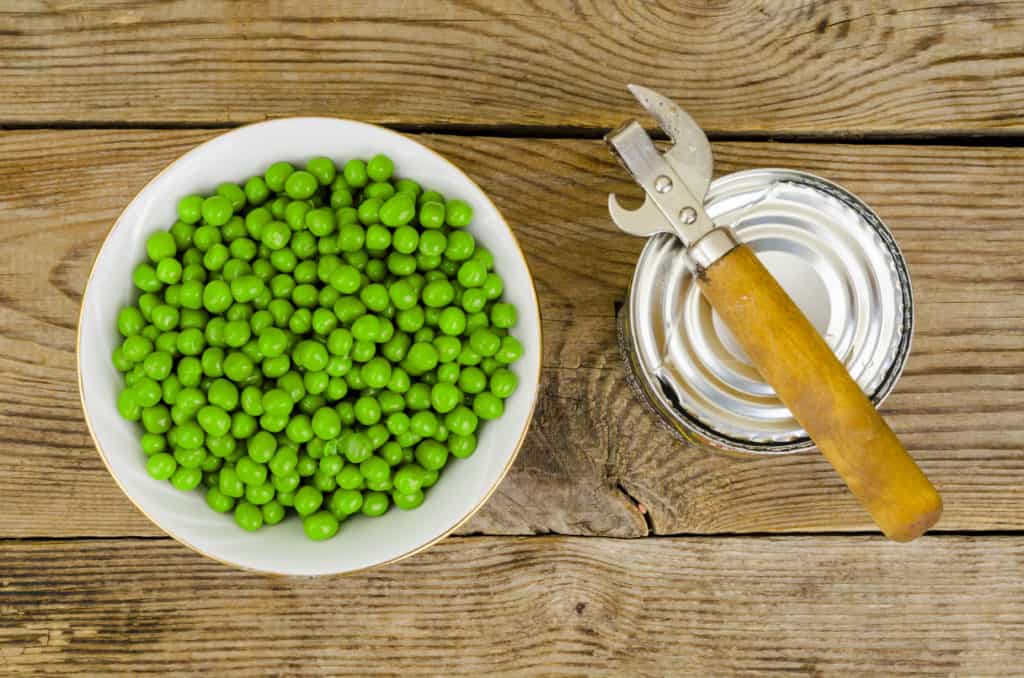 Wooden bowl with canned green peas on table. Studio Photo