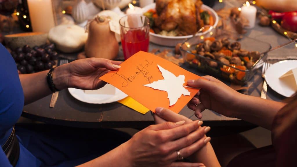 Hands exchanging a greeting card that says "thankful."