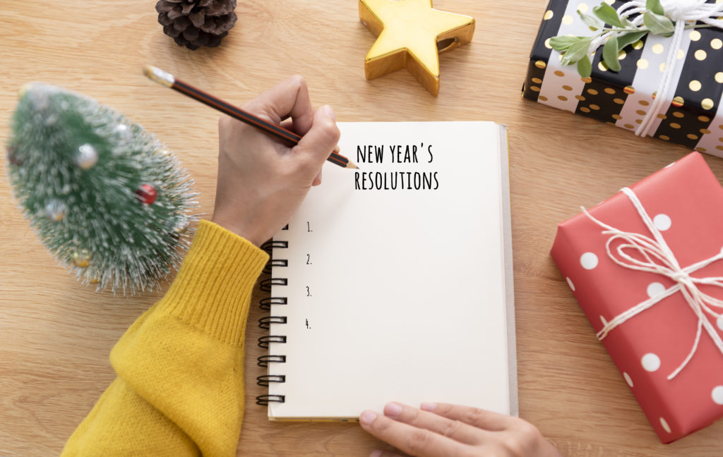 A notebook with the written title "New Year's Resolutions" with a hand poised over it to start writing